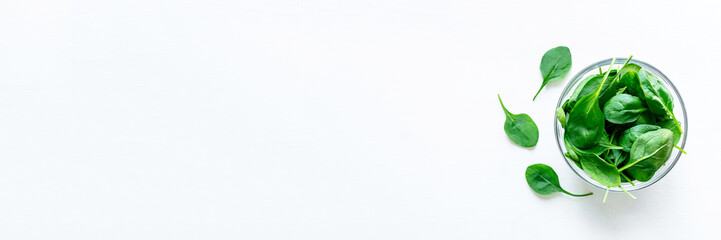 Fresh green spinach leaves in glass bowl on white table. Organic food, healthy diet, vegetarian food. Top view.