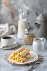 Pancakes stacked on a plate on a white table with a cup of coffee and a bottle of milk