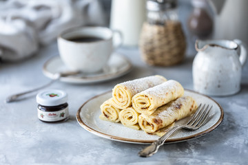 Pancakes stacked on a plate on a white table with a cup of coffee and a bottle of milk