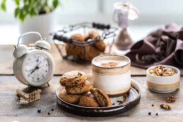 Homemade cookies with nuts and coffee in a ceramic cup on a wooden table. Time to drink some coffee. Alarm clock in the background. Breakfast