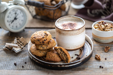 Homemade cookies with nuts and coffee in a ceramic cup on a wooden table. Time to drink some coffee. Alarm clock in the background. Breakfast