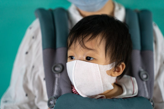 Asian baby with mother in baby carry,baby is wearing a protection mask against air pollution and Wuhan covic corona virus before flight in terminal DonMuang airport,Bangkok, Thailand.