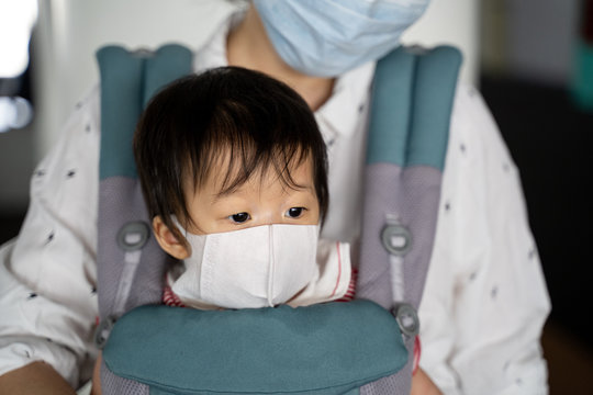 Asian baby with mother in baby carry,baby is wearing a protection mask against air pollution and Wuhan covic corona virus before flight in terminal DonMuang airport,Bangkok, Thailand.