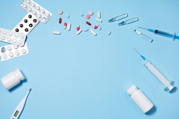 Fototapeta na wymiar Medical pills and capsules in packs, an injector syringe on blue background