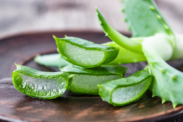 Pieces of aloe vera and fresh leaves lie on a bowl against the background of old boards.