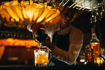 The bartender squeezes citrus juice into a cocktail.
