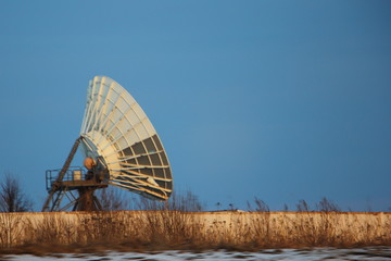 Large dish antenna behind a concrete fence on a blue sky background, TV repeater, telecommunications