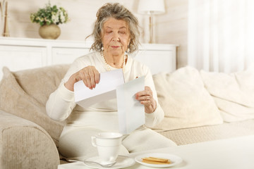 An old lady takes a letter out of a mail envelope