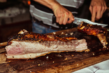 Chef hand cuts piece grilled pork in steaks with knife. Traditional suckling pig cooked on the charcoal grill. The little pig is roasted whole on an open fire. Organic pig on the spit.