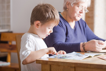 Portrait of beautiful mature woman (80 years old) with her great-grandson at home, reading educational book together
