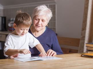Portrait of beautiful mature woman (80 years old) with her great-grandson at home, reading...