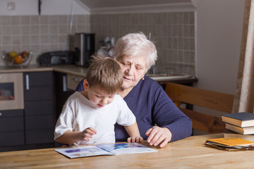 Portrait of beautiful mature woman (80 years old) with her great-grandson at home, reading...