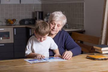 Portrait of beautiful mature woman (80 years old) with her great-grandson at home, reading...