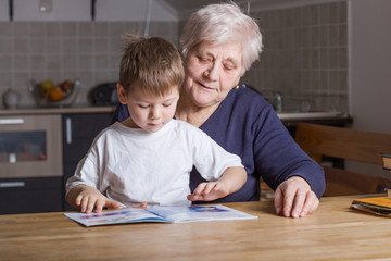 Portrait of beautiful mature woman (80 years old) with her great-grandson at home, reading...