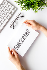 Subscribe. Advertisement in hand on white office desk top-down
