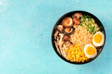 Ramen. Soba noodles with eggs, shiitake and enoki mushrooms, corn and scallions, top shot on a blue background with a place for text