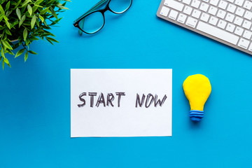 Start now. Motivative text on blue office desk top-down
