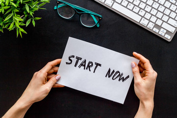 Start now. Motivative text on black office desk top-down