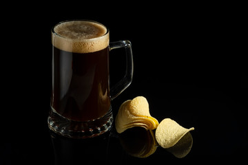 Beer in a transparent glass and potato chips on a black glass background