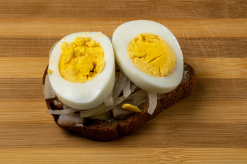 Sandwich with herring, onions and chicken egg on a wooden tray. National Russian cuisine