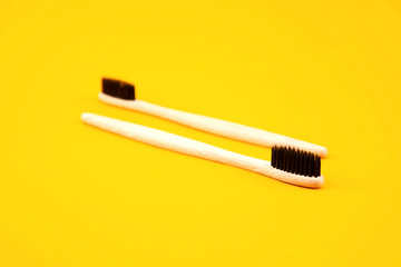 Two toothbrushes made of natural materials lie on a yellow background. Place for text. Refusal of plastic. Zero waste. Oral care