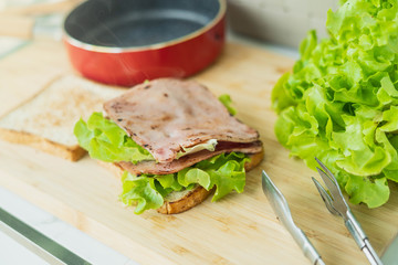 Tasty and fresh sandwiches in kitchen room. Man prepares lunch, serves grilled bread sandwich snack on top of wooden cutting board.