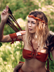 Beautiful girl archer with long blond hair with a bow and arrows dressed in leather