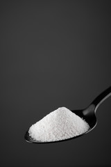 collagen powder in black spoon. grey background closeup. Natural beauty and health supplement