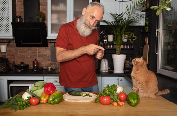 Portrait of handsome bearded senior man talking with cat in the kitchen.