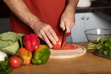 Chef's hands cutting red fresh tomato on a wooden board.