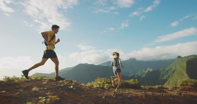 Young adventurous man and woman running together outdoors on an epic mountain top with lush green mountains in the background, amazing outdoors exploring
