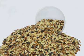 Brown, red and black rice mix on white background with plastic glass. Selective focus.