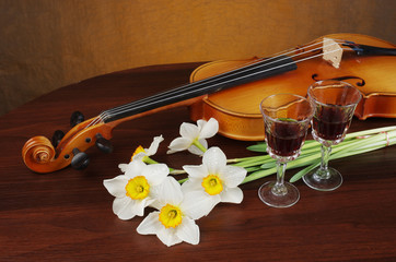 Violin with a bow, a bouquet of white daffodils and two glasses of wine on a wooden table.