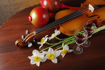 Violin with a bow, a bouquet of white daffodils and two glasses of wine on a wooden table.