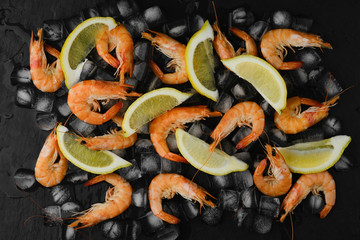 Fresh Prawns Shrimps with lemon in ice on black background. top view