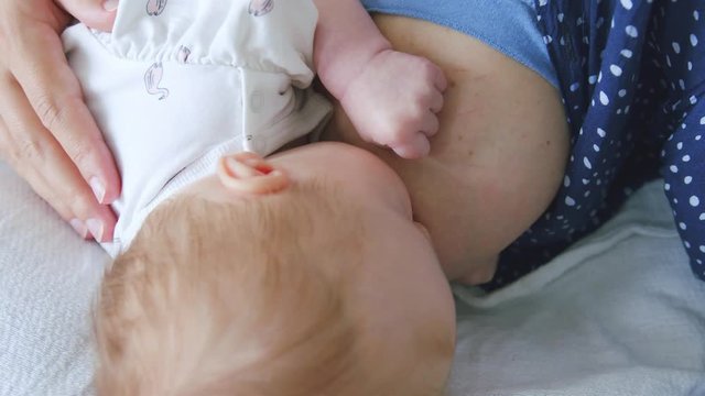 Adorable breastfeeding baby gets their back stroked to encourage a healthy long feed and good latch, while swallowing milk