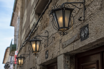 Detailed view of classic stone facade with three street retro wall lamps, on metal material, ornamented and with light on