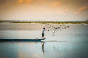Fototapeta na wymiar Fisherman standing on a wooden boat sowing nets