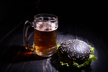 Black burger and glass of beer isolated on black