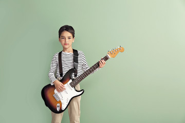 Little boy playing guitar on color background