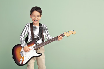 Little boy playing guitar on color background