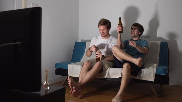 Two Male Friends Drinking Beers While Watching Sports on TV
