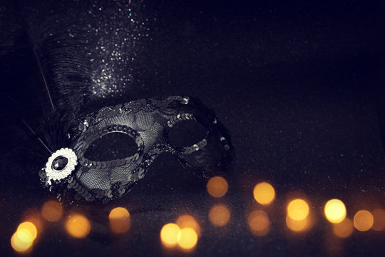 Photo of elegant and delicate black Venetian mask over dark glitter background