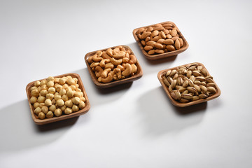 Hazelnuts, almonds, pistachios and cashews in the wooden bowls on white background with copy space