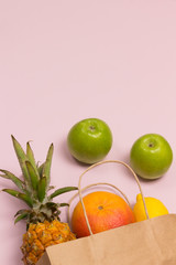 Paper bag with fruit containing collagen vitamins on pink background: apple lemon grapefruit pineapple