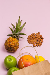 Paper bag with fruit containing collagen vitamins on pink background: apple lemon grapefruit pineapple nuts