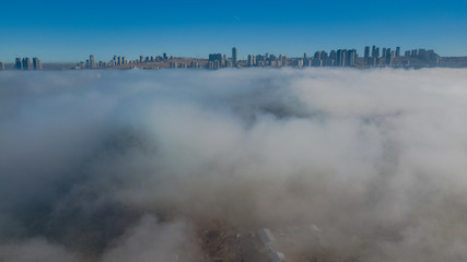 Fototapeta na wymiar Landscape over the clouds in foggy weather. Hills of buildings in foggy weather. The drone and the top of the fog layer. Buildings in the fog.