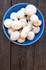Fresh white Champignon mushrooms  on vintage wood table background. In a blue bowl