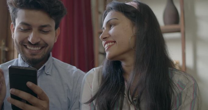 Indian couple discuss and buy online together as they share their smart phone mobile phone using their bank debit cards and celebrate with high five their hands, slow-motion handheld 60 fps