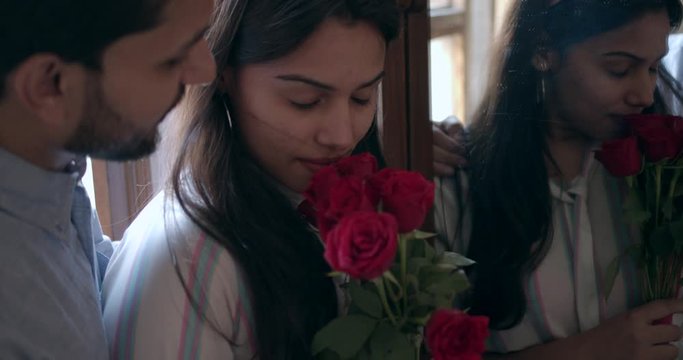 Hand-held closeup mid shot of a lovely young Indian couple embracing sharing hugging holding and smelling red roses celebration for their anniversary birthday and valentine's day in slow-motion 60 fps